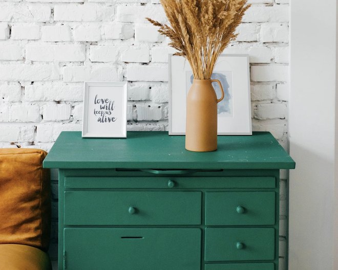 turqoise drawers with picture frames and a vase on top all infront of a white brick wall